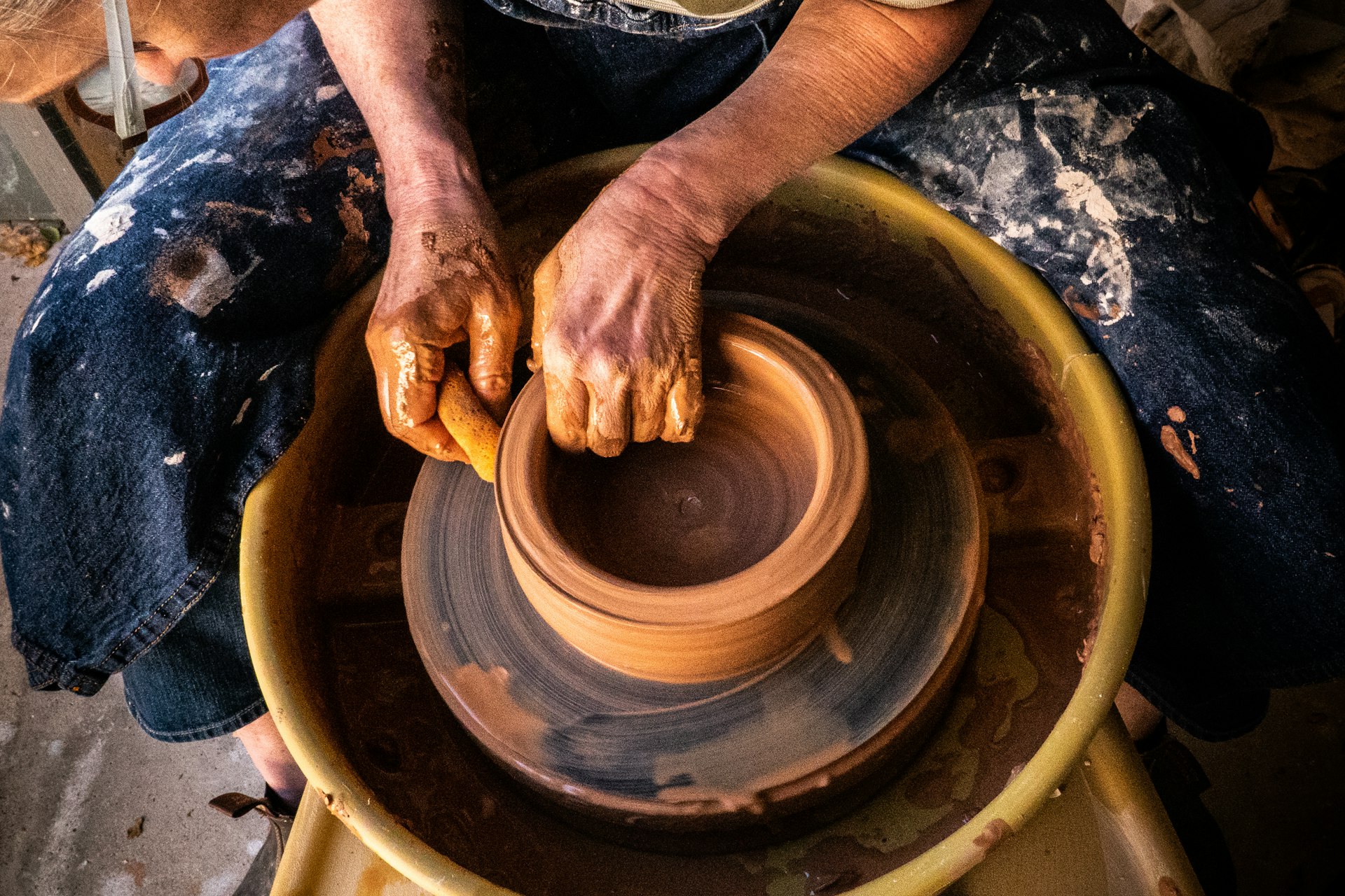 A potter's hands shaping a clay bowl on a spinning wheel in a studio